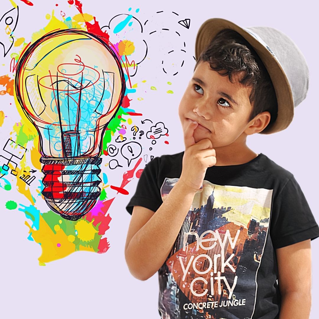 Young boy wearing a t-shirt and a hat doing a thinking pose. A brightly coloured lightbulb with paint splatters and doodles is next to him.