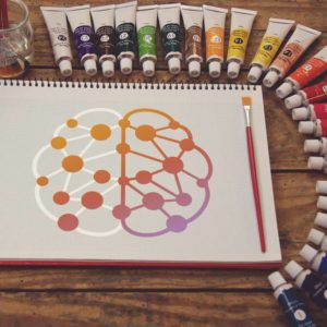 NeuroTribe UK logo painted onto a sketchpad, next to a red paintbrush and tubes of paint